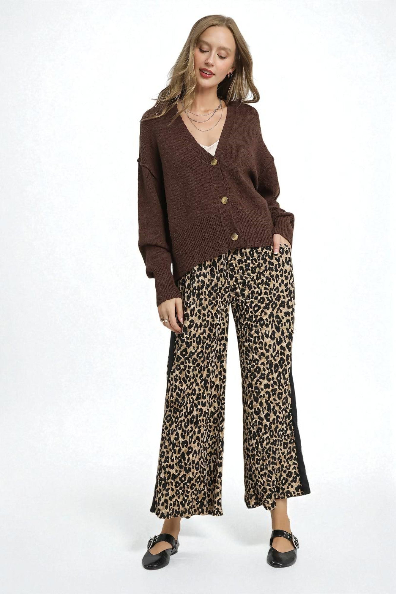 Woman wearing a brown cardigan and leopard print pants on a white background