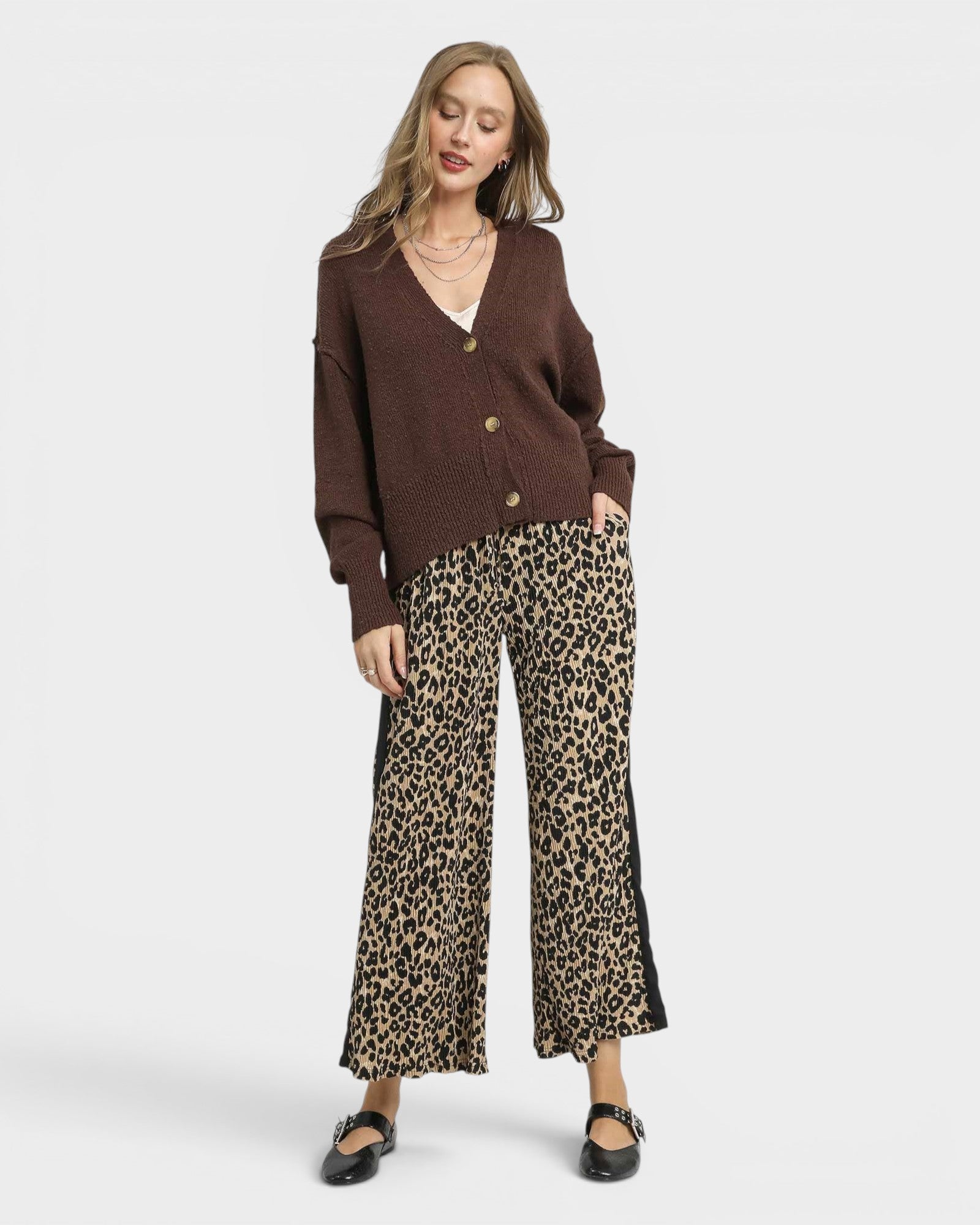 Woman wearing a brown cardigan and leopard print pants on a white background