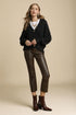 Woman wearing a black sweater, white shirt, brown leather pants, and brown boots on a beige background