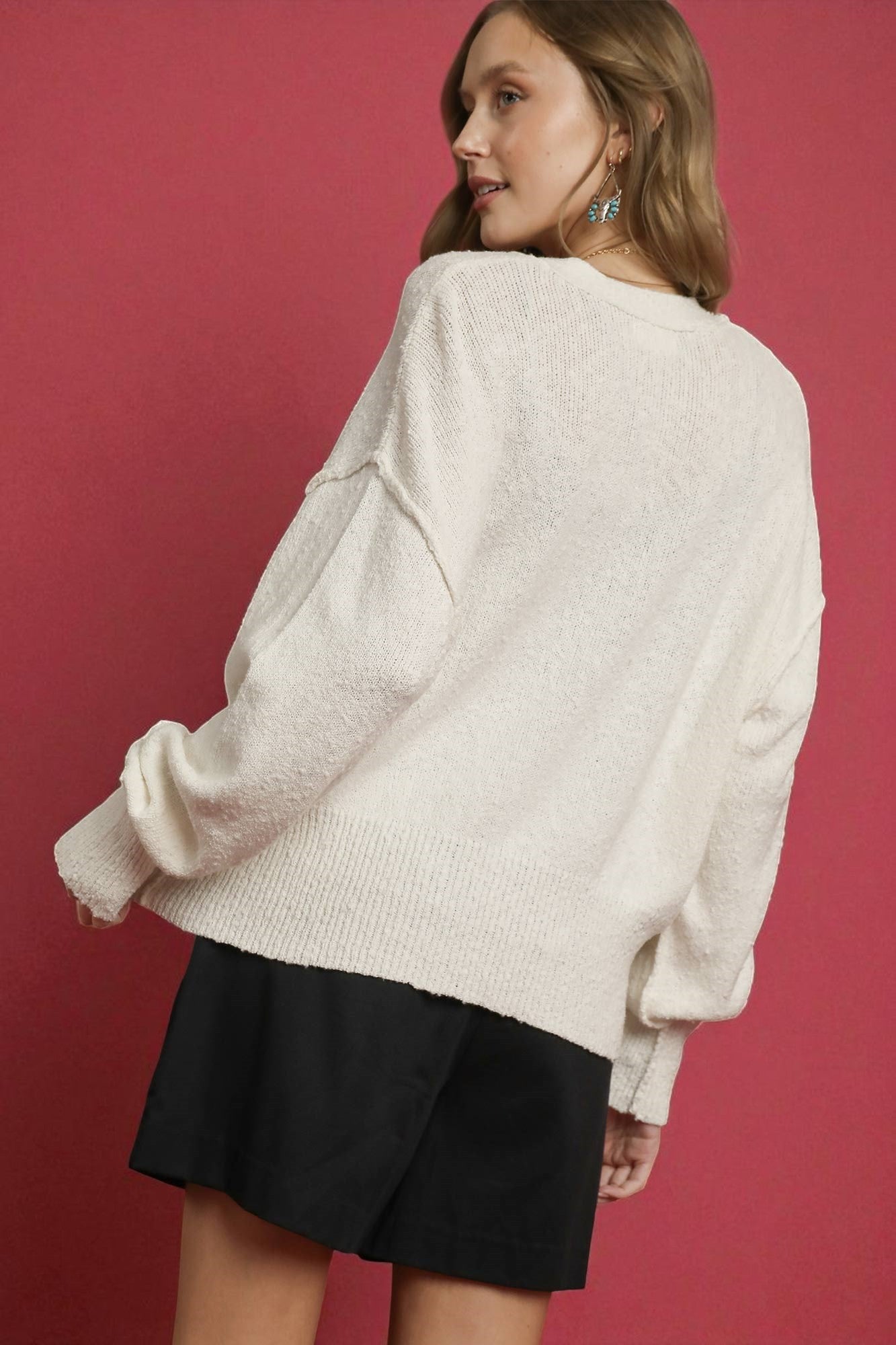 Person wearing a white sweater and black skirt against a red background