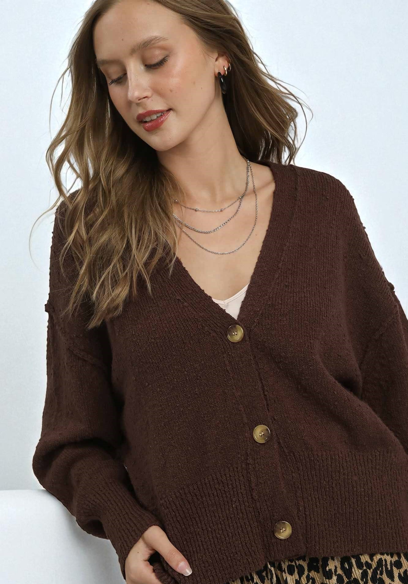 Woman wearing a brown cardigan with gold buttons on a white background