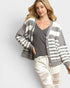 Woman wearing a gray and white striped cardigan over a gray shirt and white pants on a light background