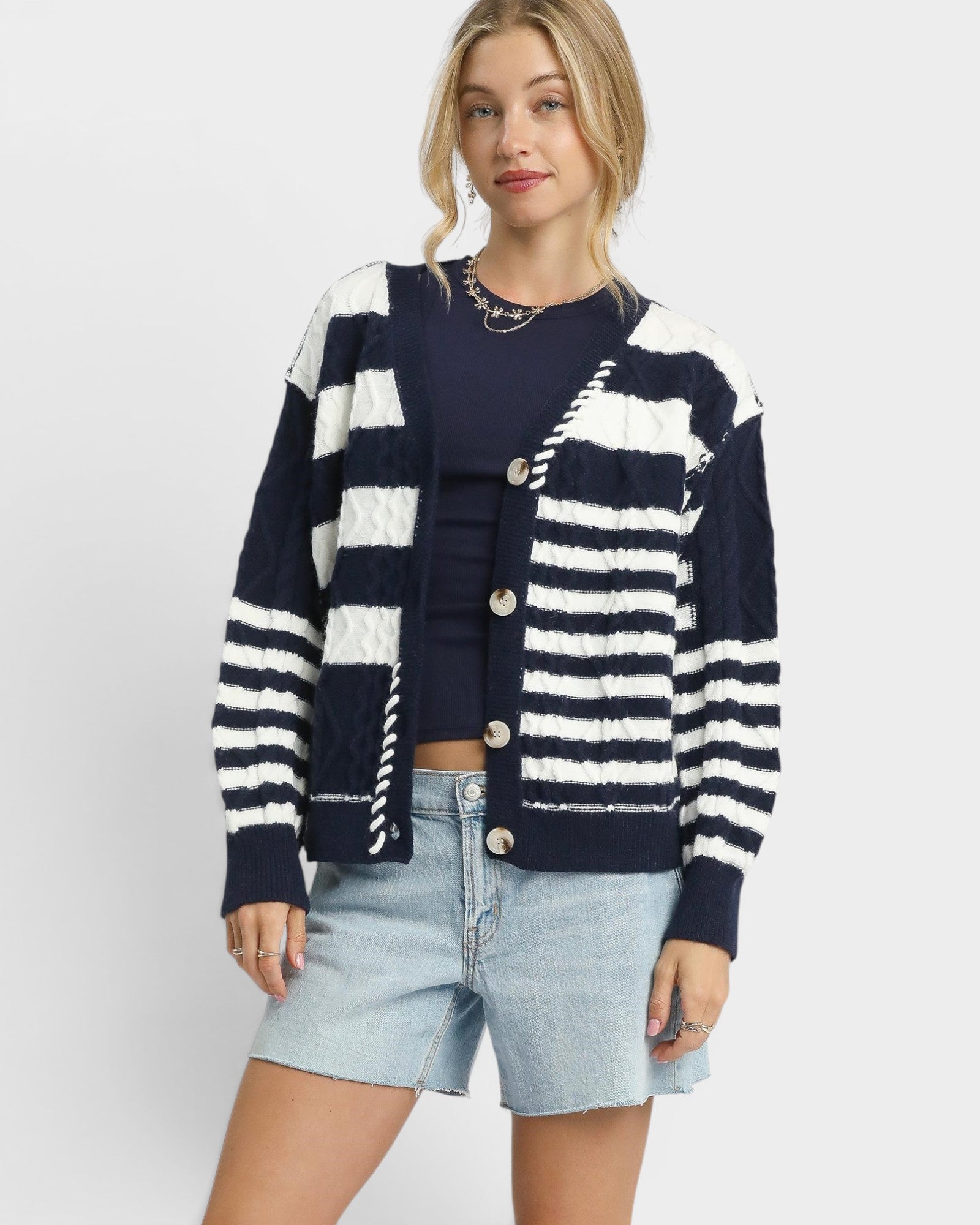 Woman wearing a navy and white striped cardigan over a dark top and denim shorts on a white background