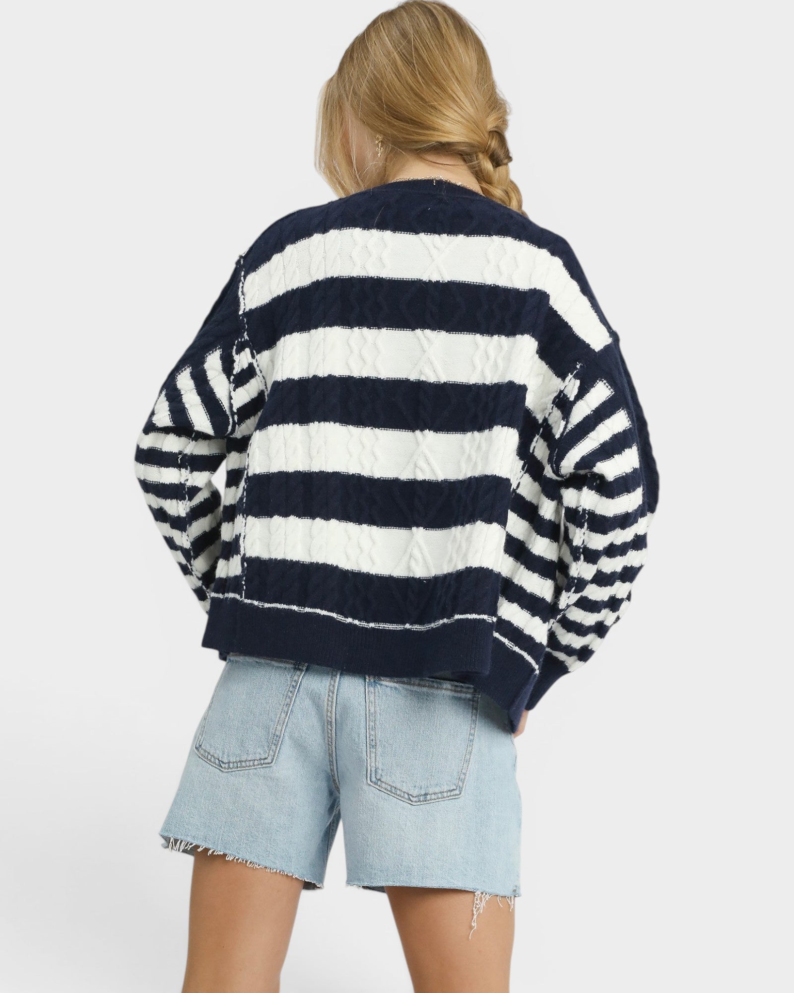 Person wearing a navy and white striped sweater with denim shorts on a plain background