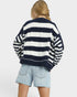 Person wearing a navy and white striped sweater with denim shorts on a plain background