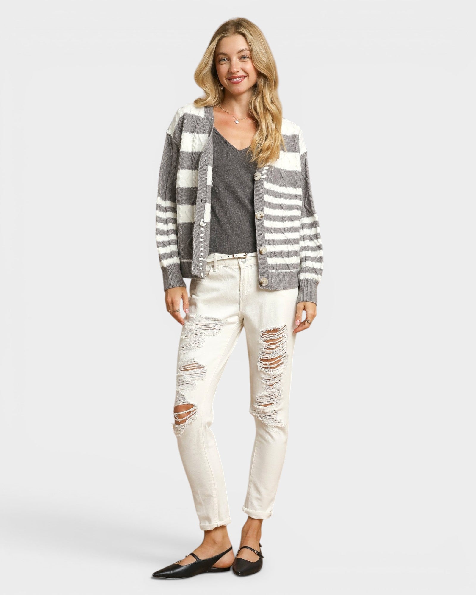 Woman wearing a striped cardigan, gray shirt, and white distressed jeans on a plain background