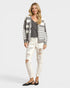 Woman wearing a striped cardigan, gray shirt, and white distressed jeans on a plain background