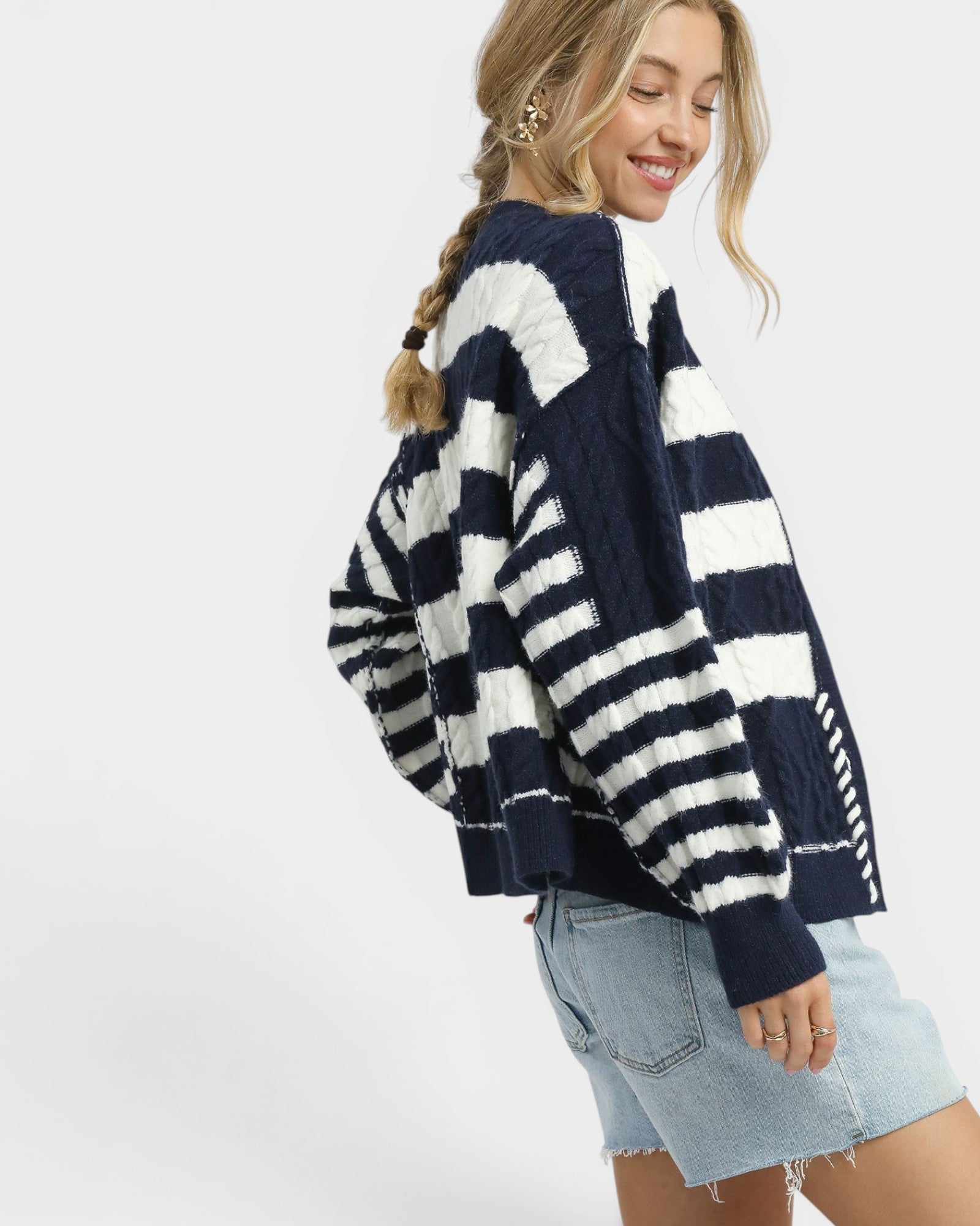 Woman wearing a navy and white striped sweater with denim shorts on a white background