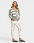 Woman wearing a gray and white striped sweater with white pants on a light gray background