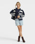 Woman wearing a navy and white striped cardigan over a dark top with denim shorts and brown boots on a white background