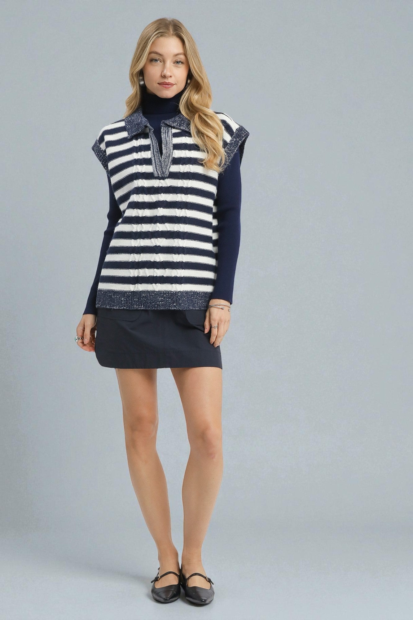 Woman wearing a navy and white striped sweater vest over a black dress on a gray background