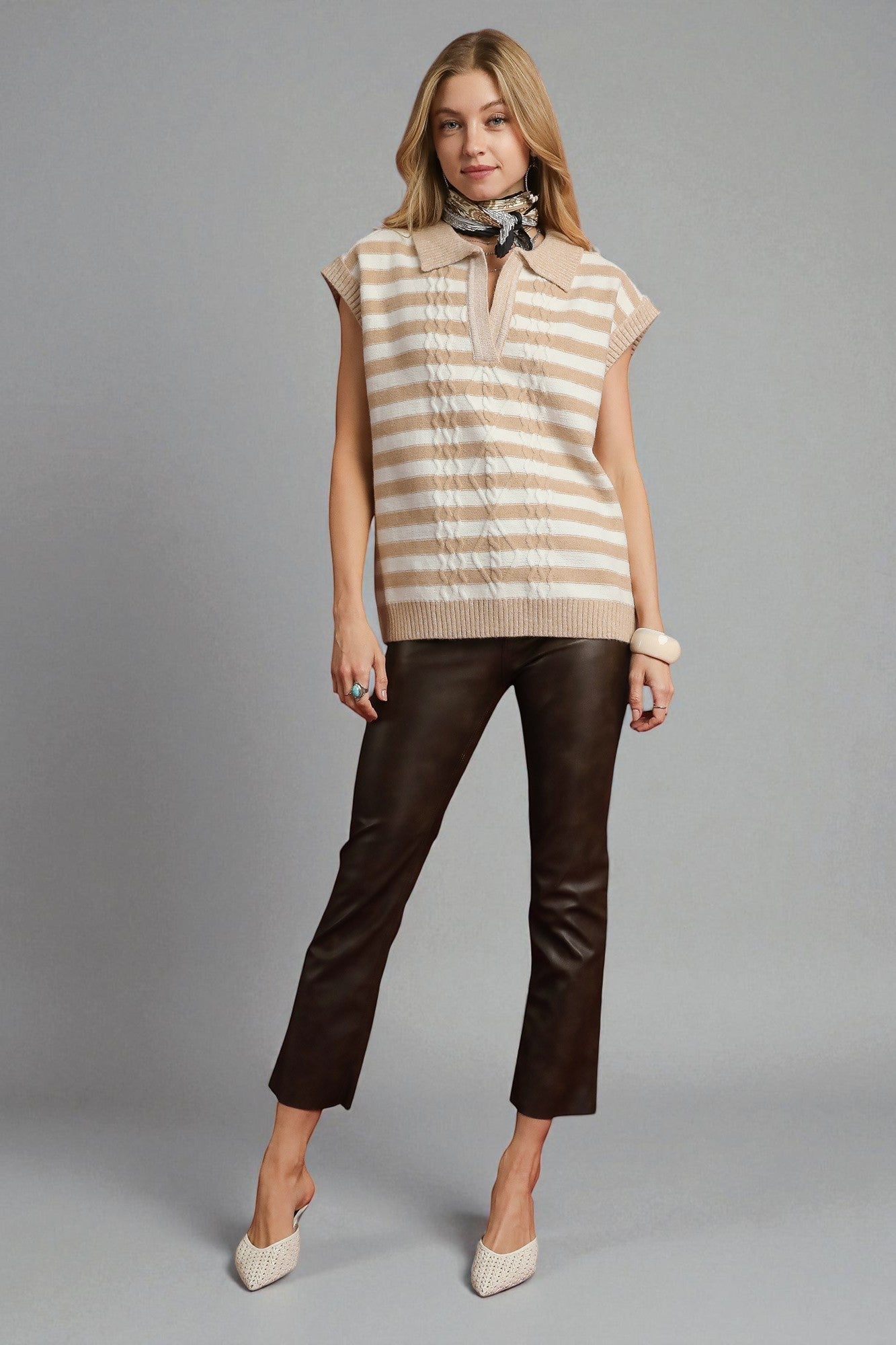 Woman wearing a striped sleeveless top and brown pants on a gray background