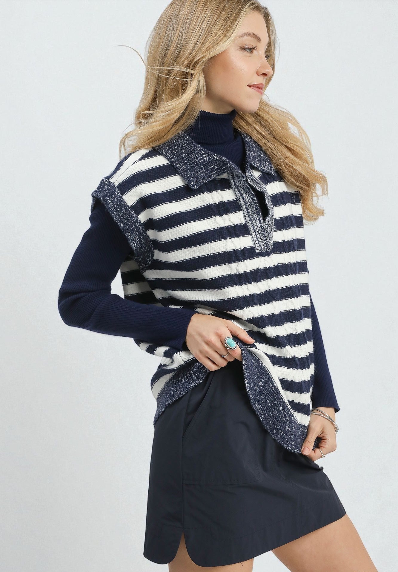 Woman wearing a navy and white striped vest over a dark blue top and black skirt on a white background.