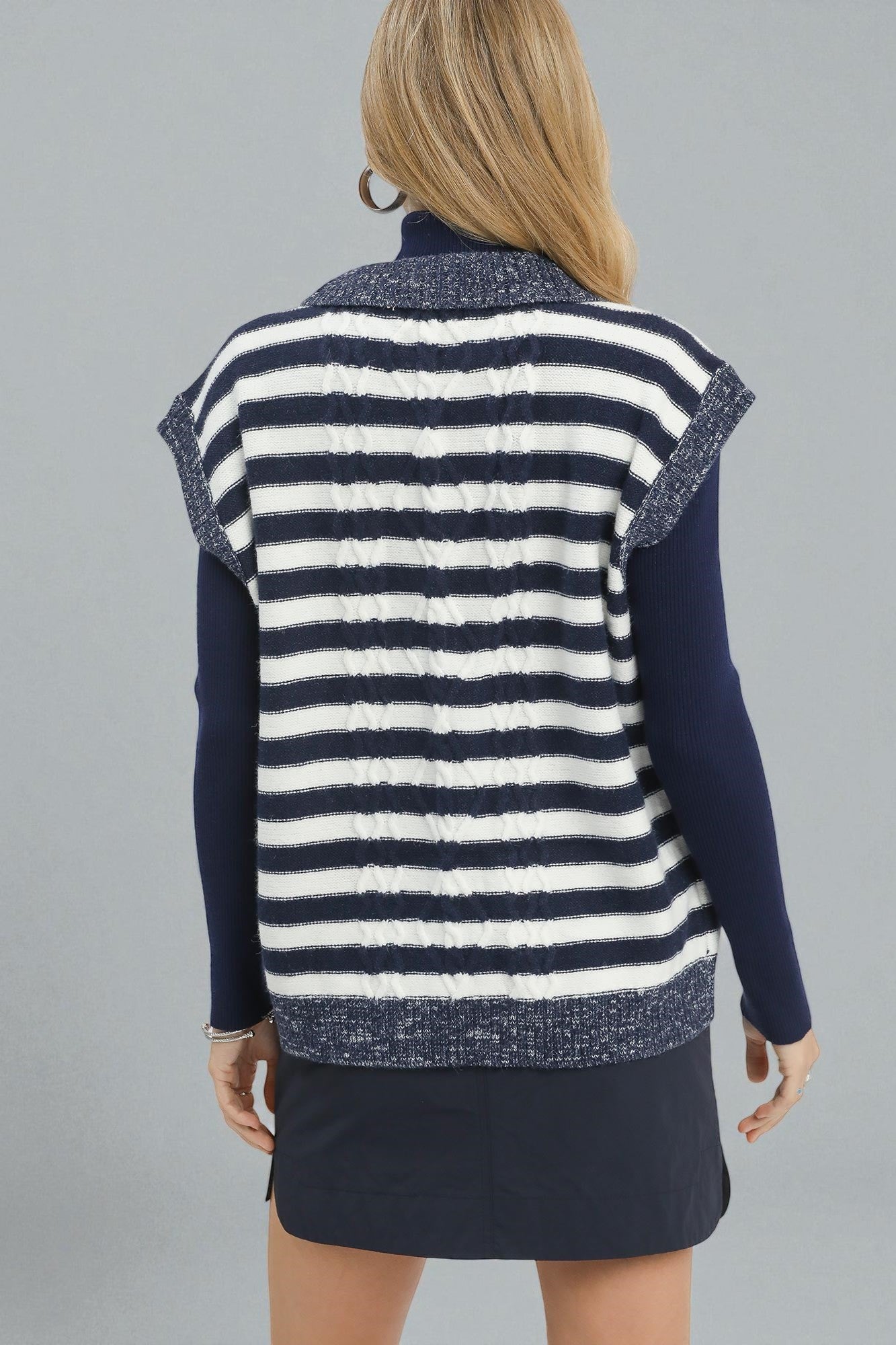 Woman wearing a navy and white striped vest over a dark blue long-sleeve shirt on a gray background