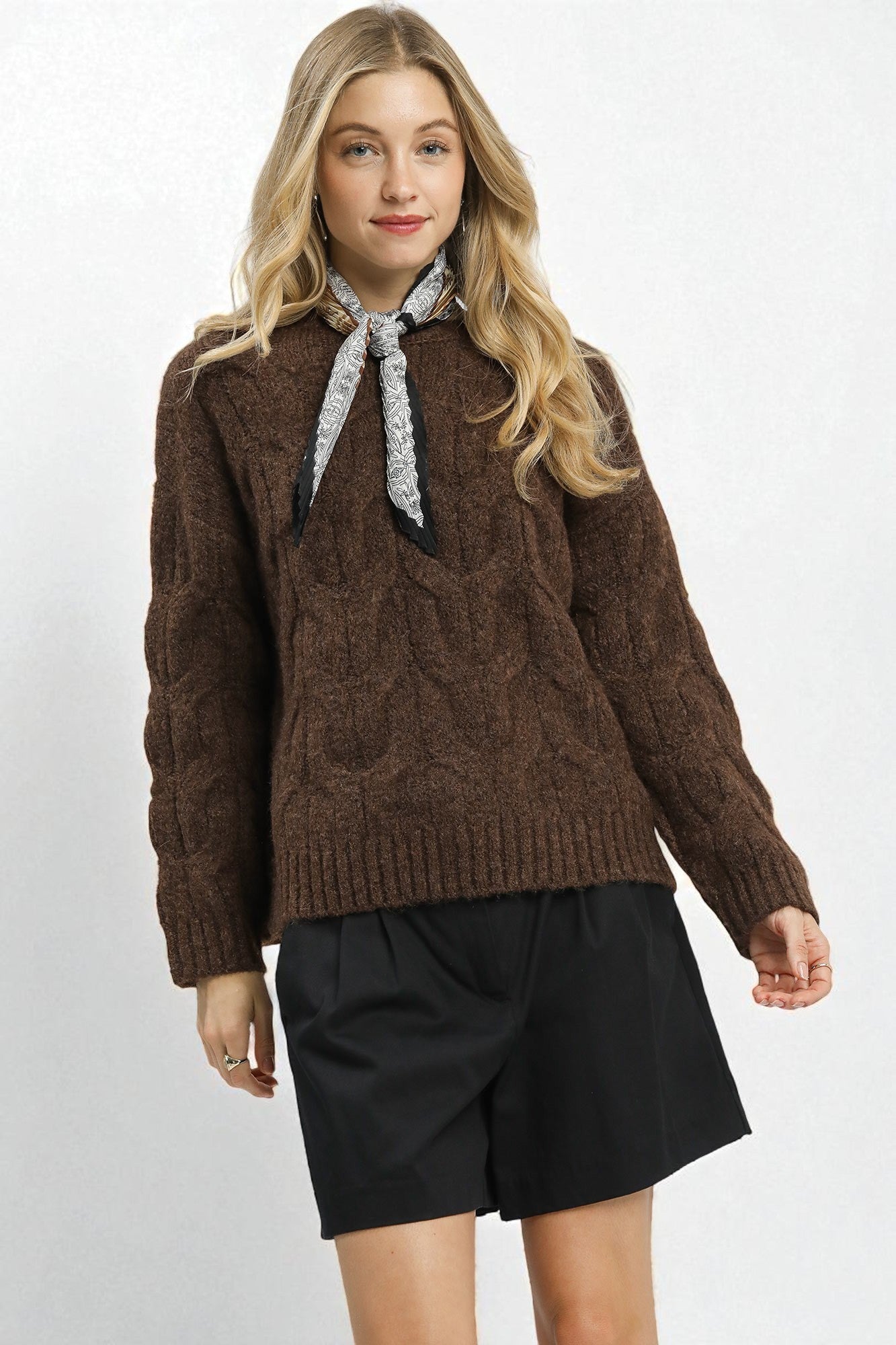 Woman wearing a brown sweater with a bow tie and black shorts on a white background