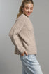 Woman wearing a beige knitted sweater and light blue jeans against a gray background