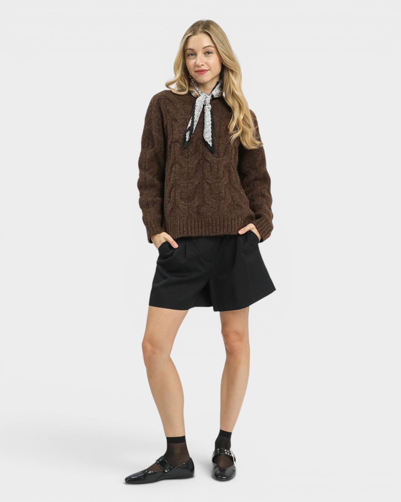 Woman wearing a brown cable knit sweater and black skirt on a white background