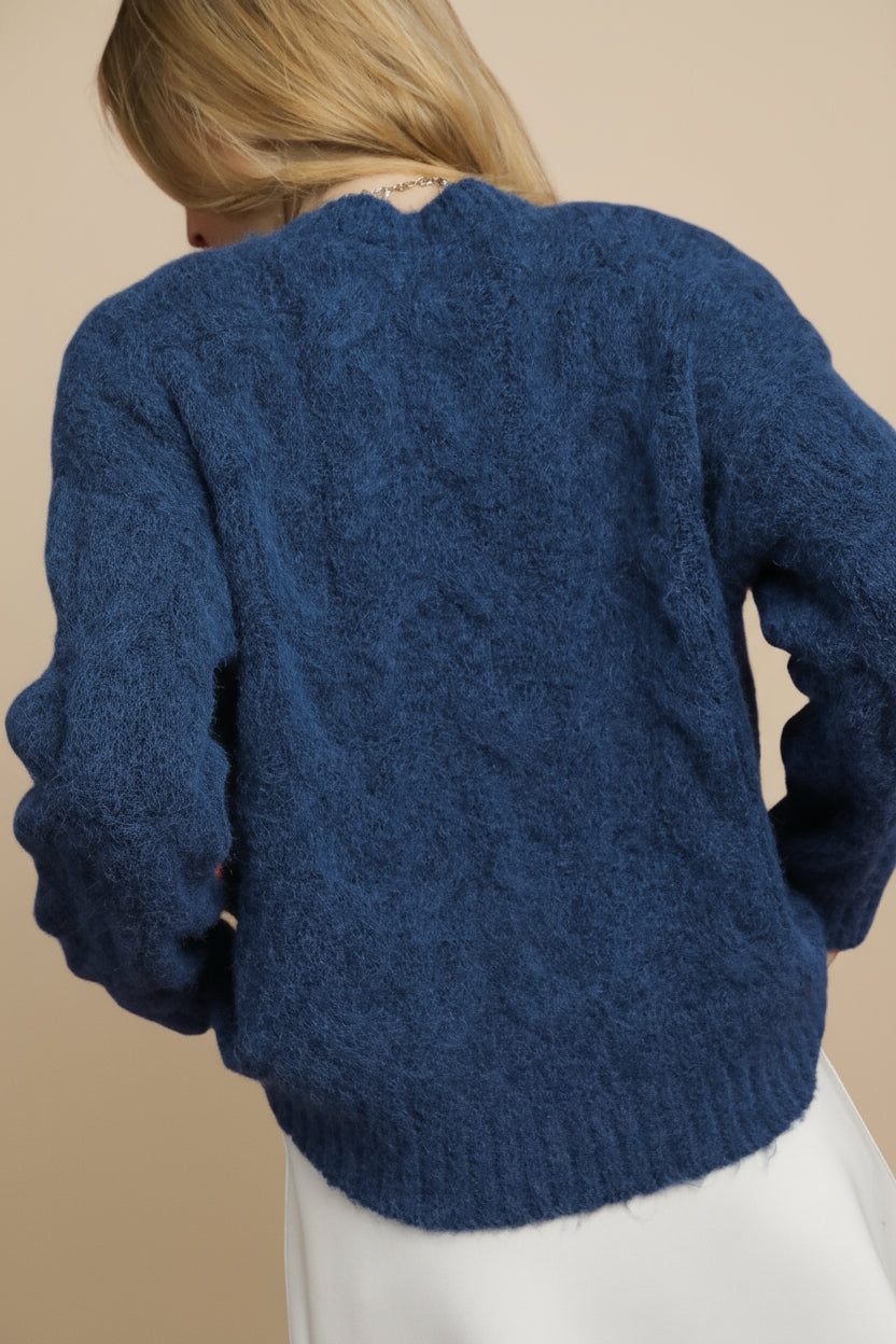Blue knitted sweater worn by a person on a plain background