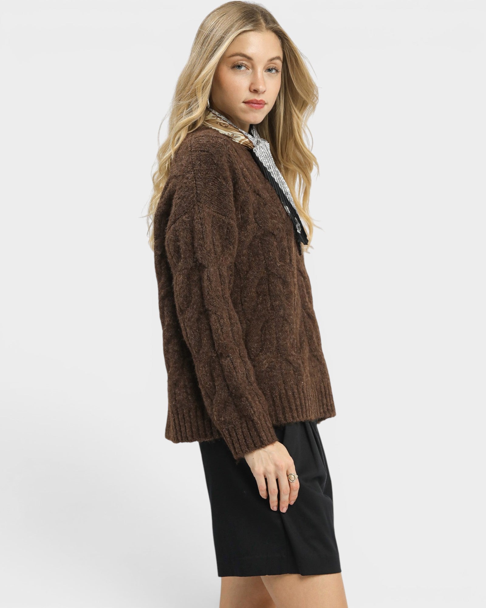Woman wearing a brown cable knit sweater on a white background
