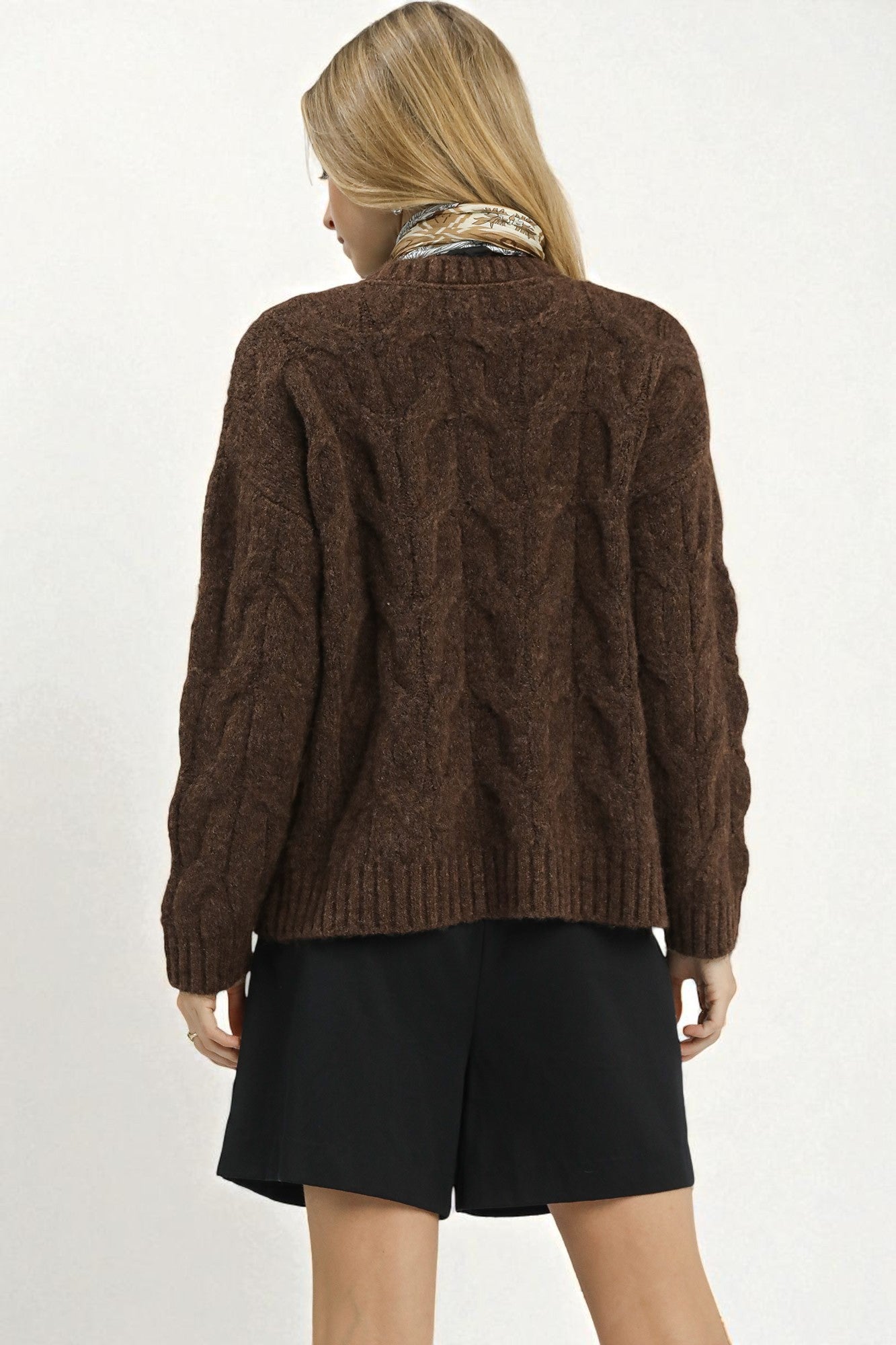 Person wearing a brown cable knit sweater and black shorts on a white background
