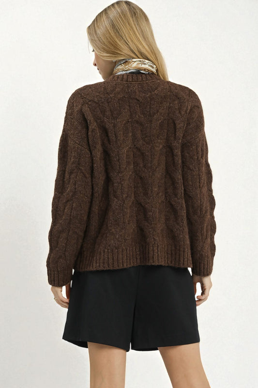 Person wearing a brown cable knit sweater and black shorts on a white background