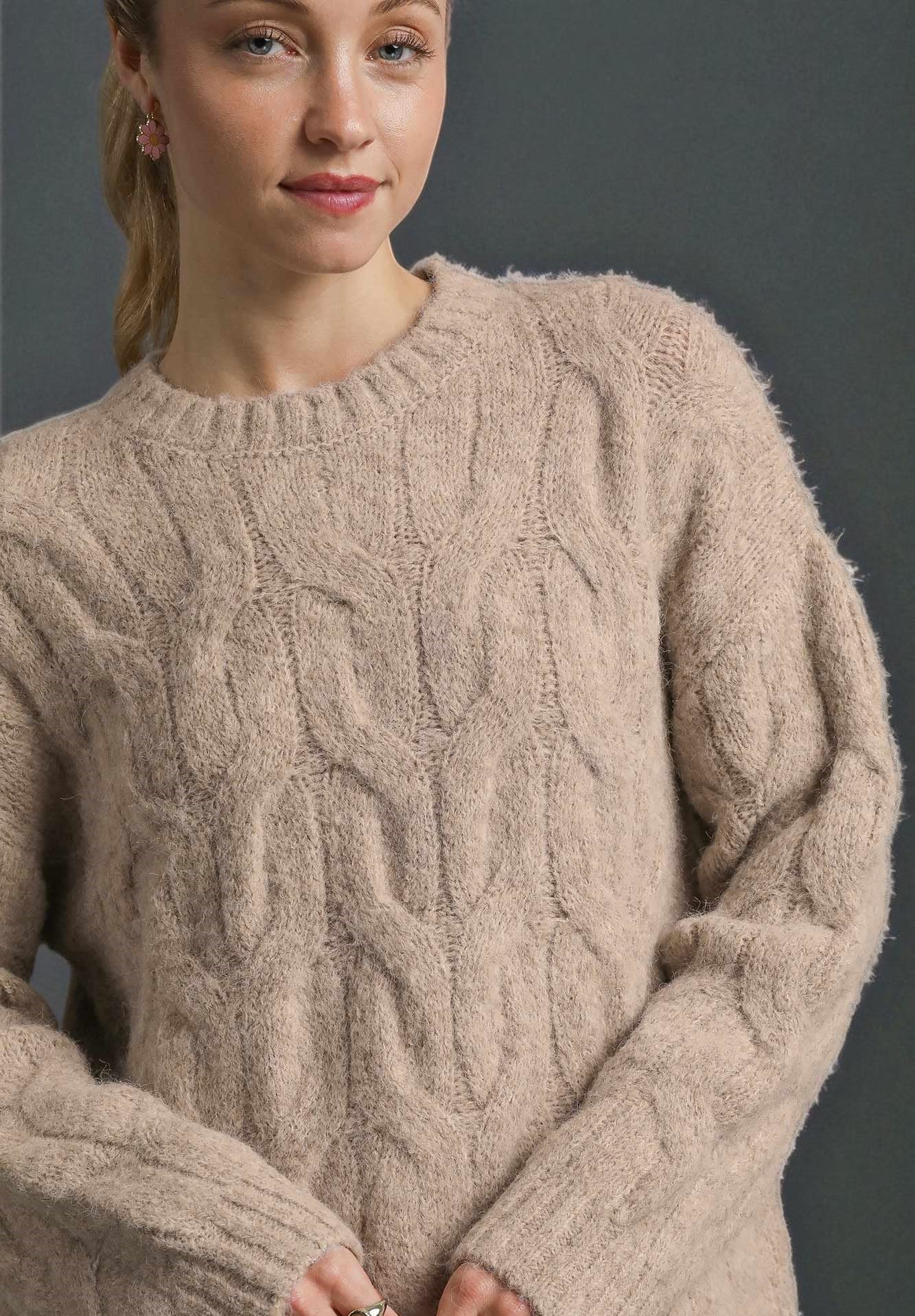 Woman wearing a beige cable knit sweater against a dark background