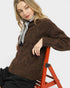 Woman wearing a brown sweater sitting on a red stool against a white background