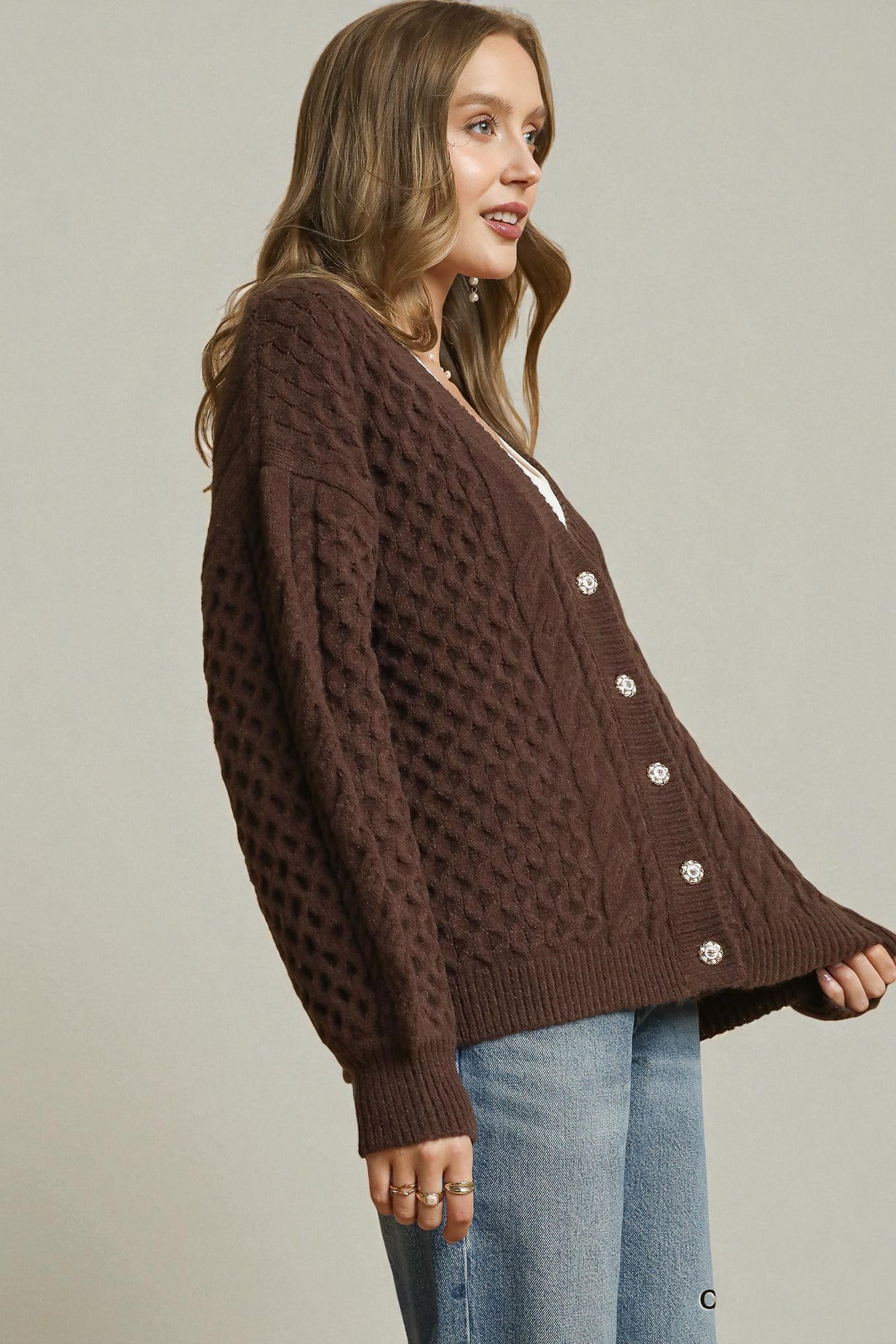 Woman wearing a brown knitted cardigan with button details on a plain background