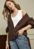 Woman wearing a brown cardigan over a white top and blue jeans.