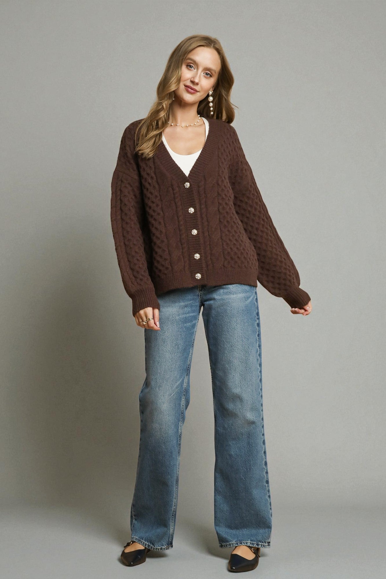 Woman wearing a brown cardigan and blue jeans against a gray background