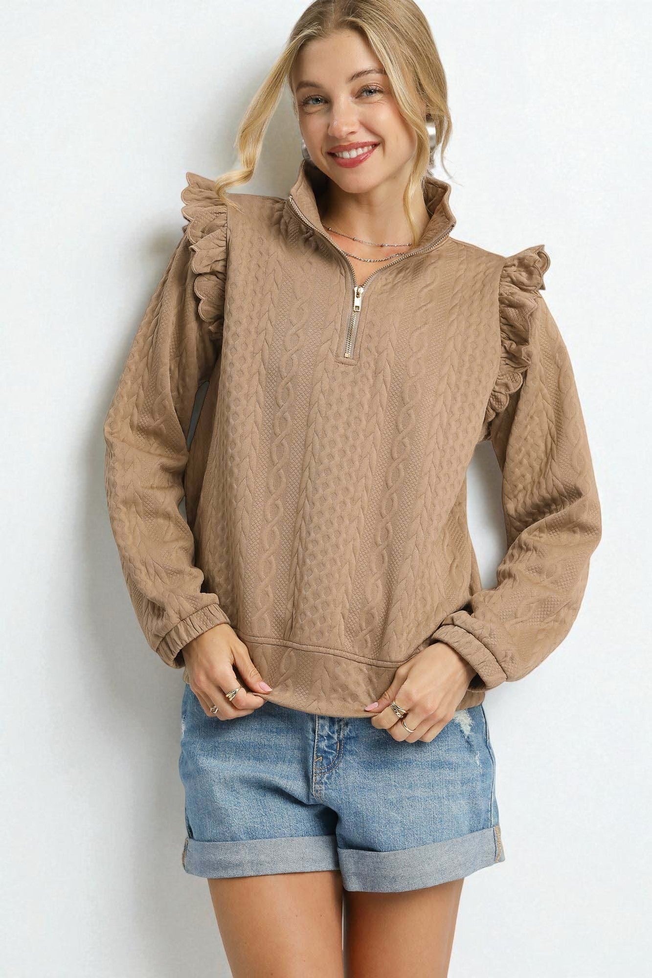 Woman wearing a brown ruffled sweater and denim shorts on a white background