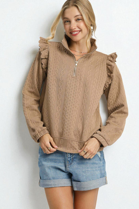 Woman wearing a brown ruffled sweater and denim shorts on a white background