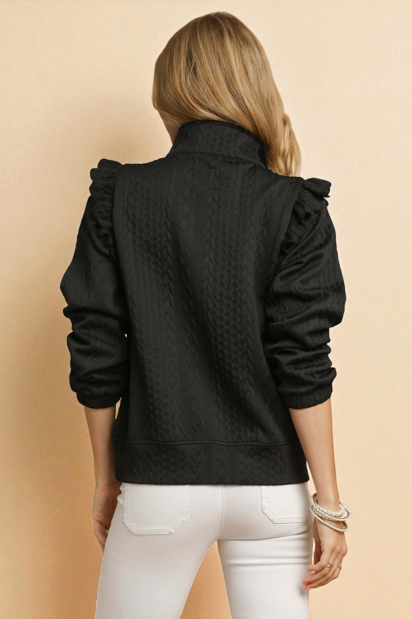 Person wearing a black textured jacket with ruffled shoulders on a beige background