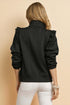Person wearing a black textured jacket with ruffled shoulders on a beige background