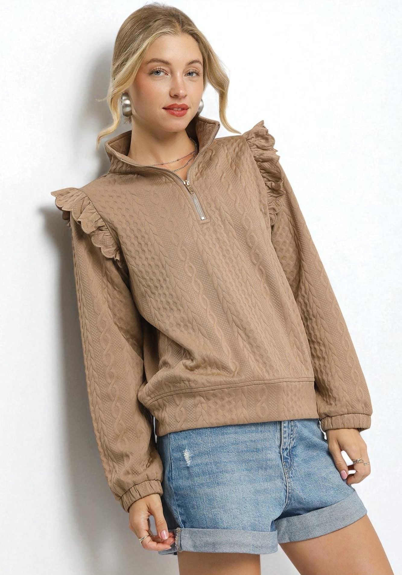 Woman wearing a beige pullover with ruffled shoulders and denim shorts on a white background