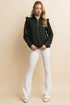 Woman wearing a black zip-up sweatshirt and white flared jeans on a beige background