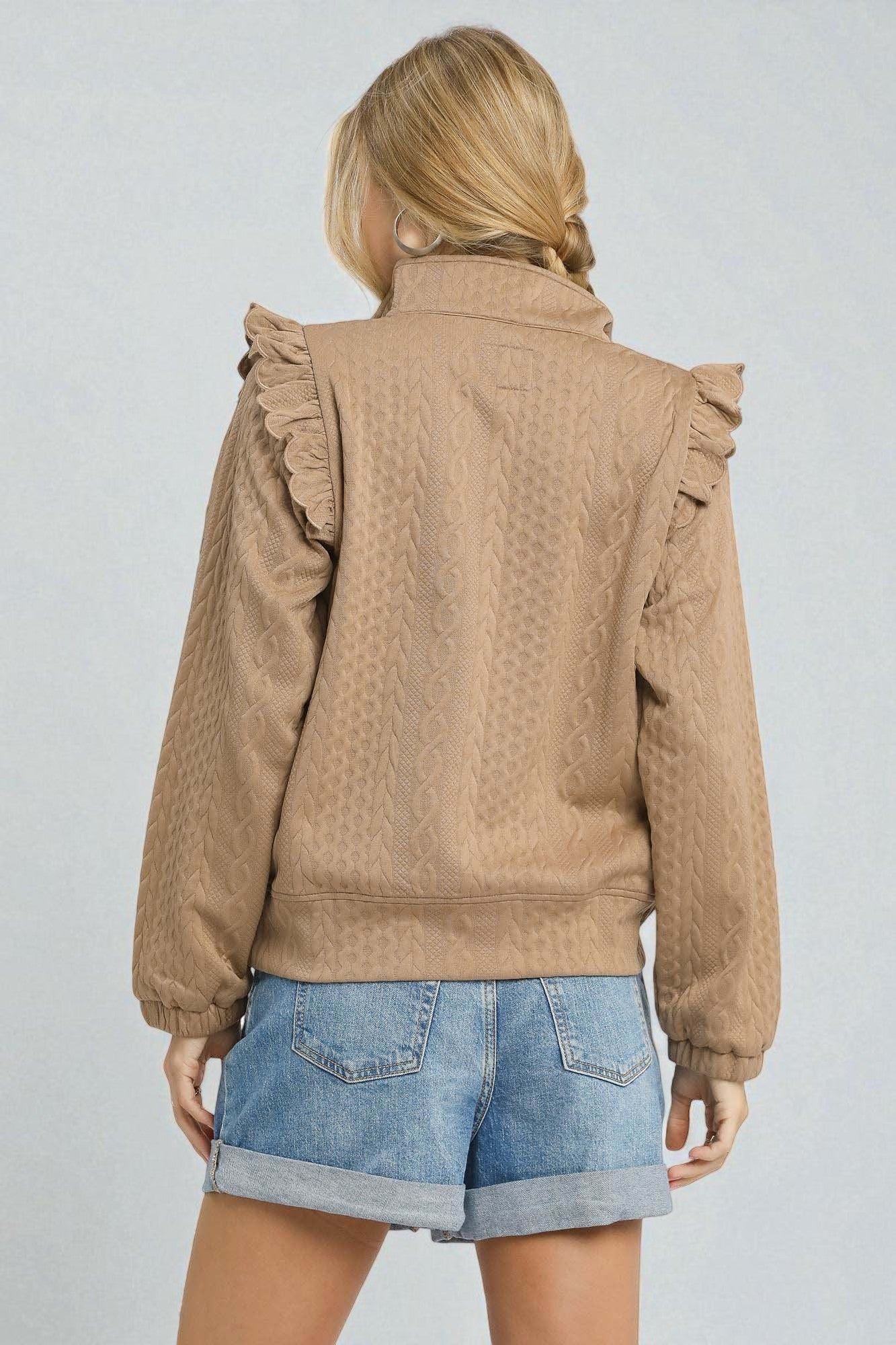 Person wearing a brown jacket with ruffled shoulders on a plain background