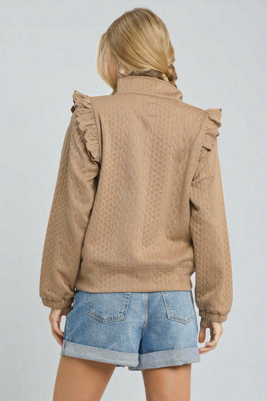 Person wearing a brown jacket with ruffled shoulders on a plain background