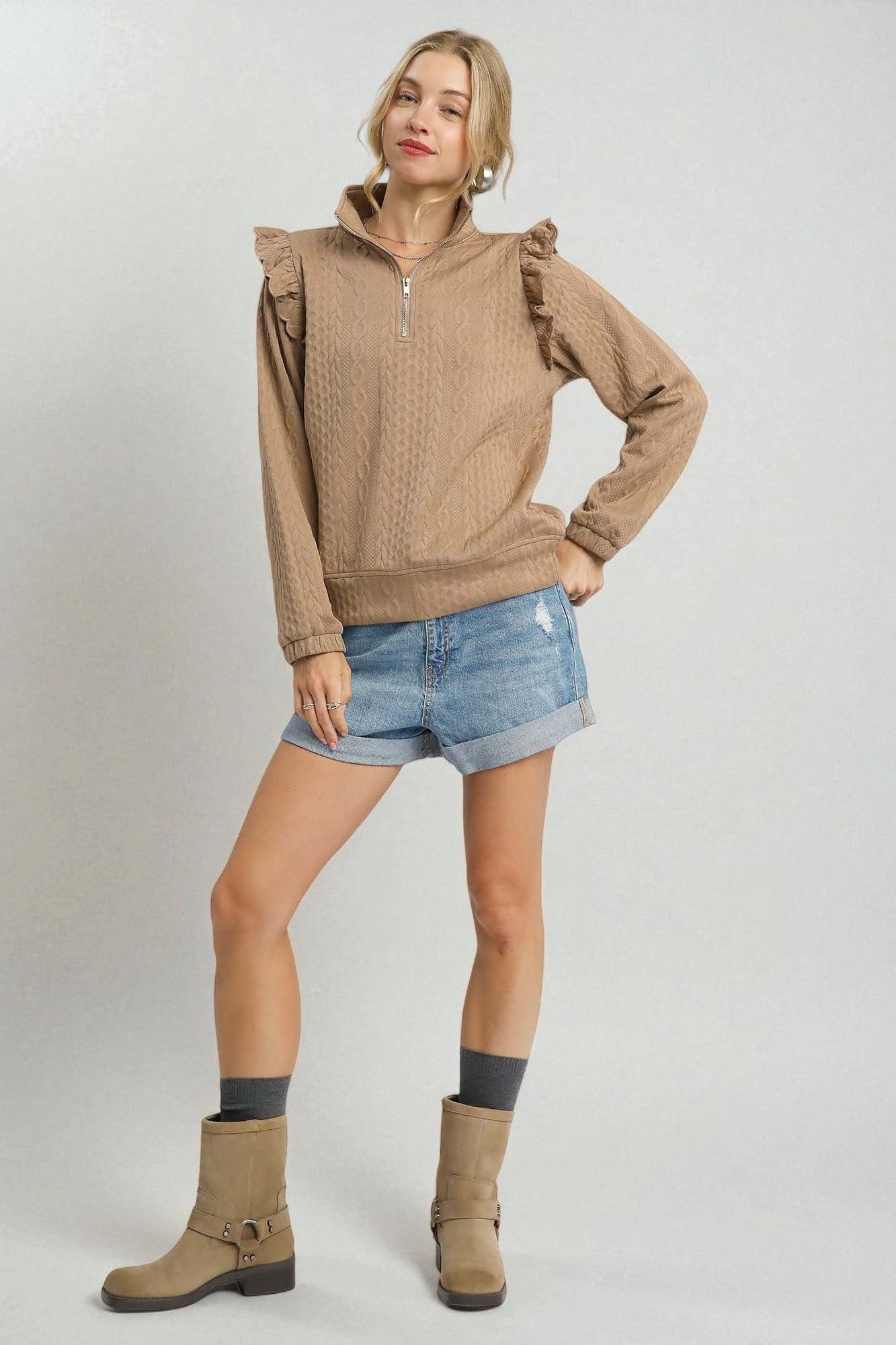 Woman wearing a brown hoodie, denim shorts, and tan boots on a white background