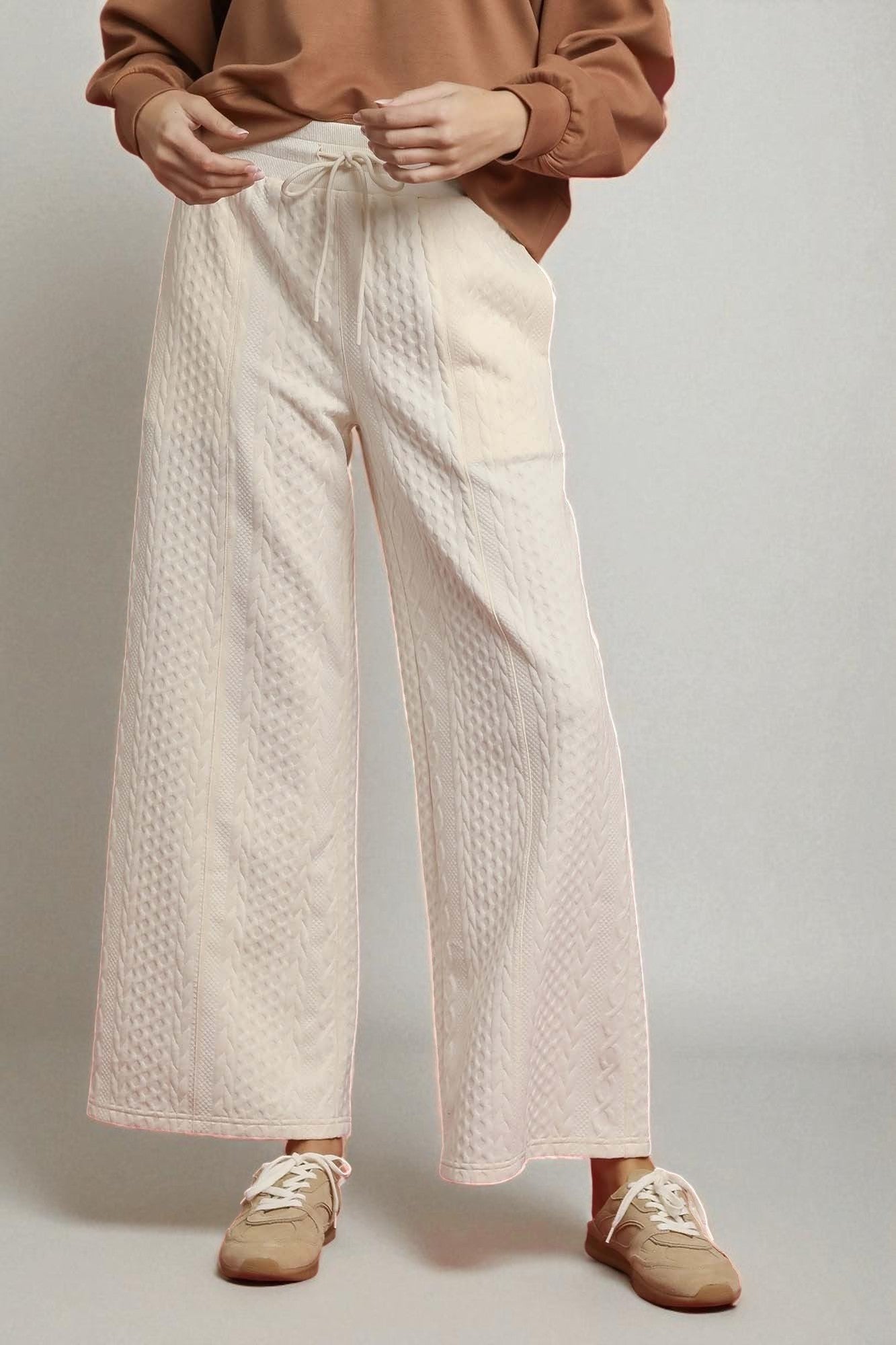 Person wearing beige quilted pants and brown shoes on a plain background