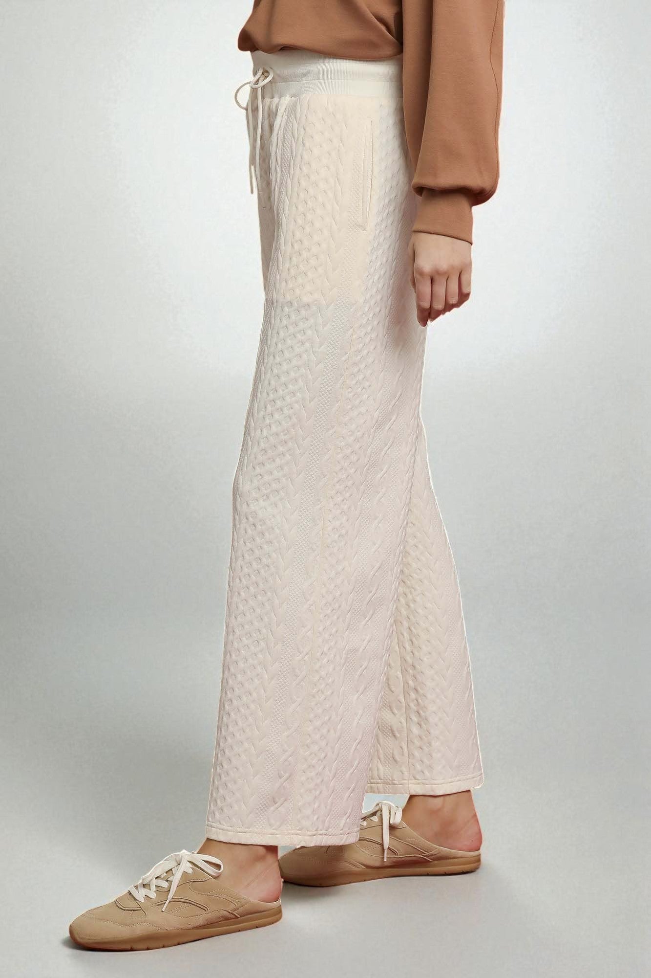 Person wearing beige quilted pants and brown shoes on a light gray background