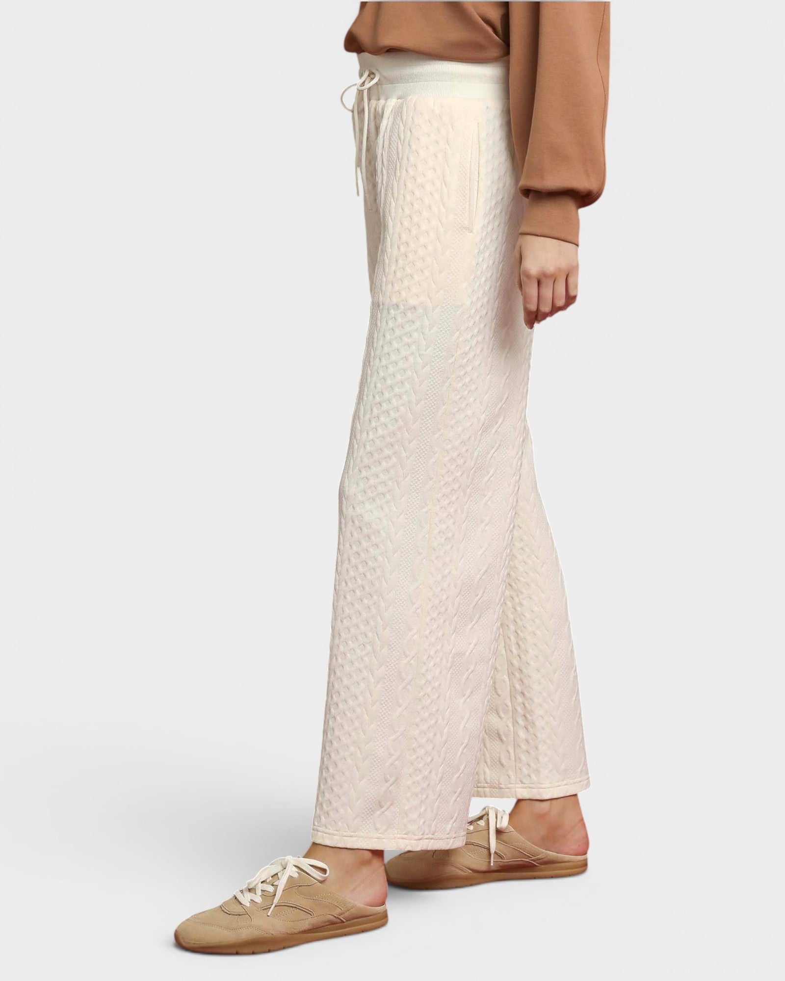 Person wearing beige quilted pants and brown shoes on a white background