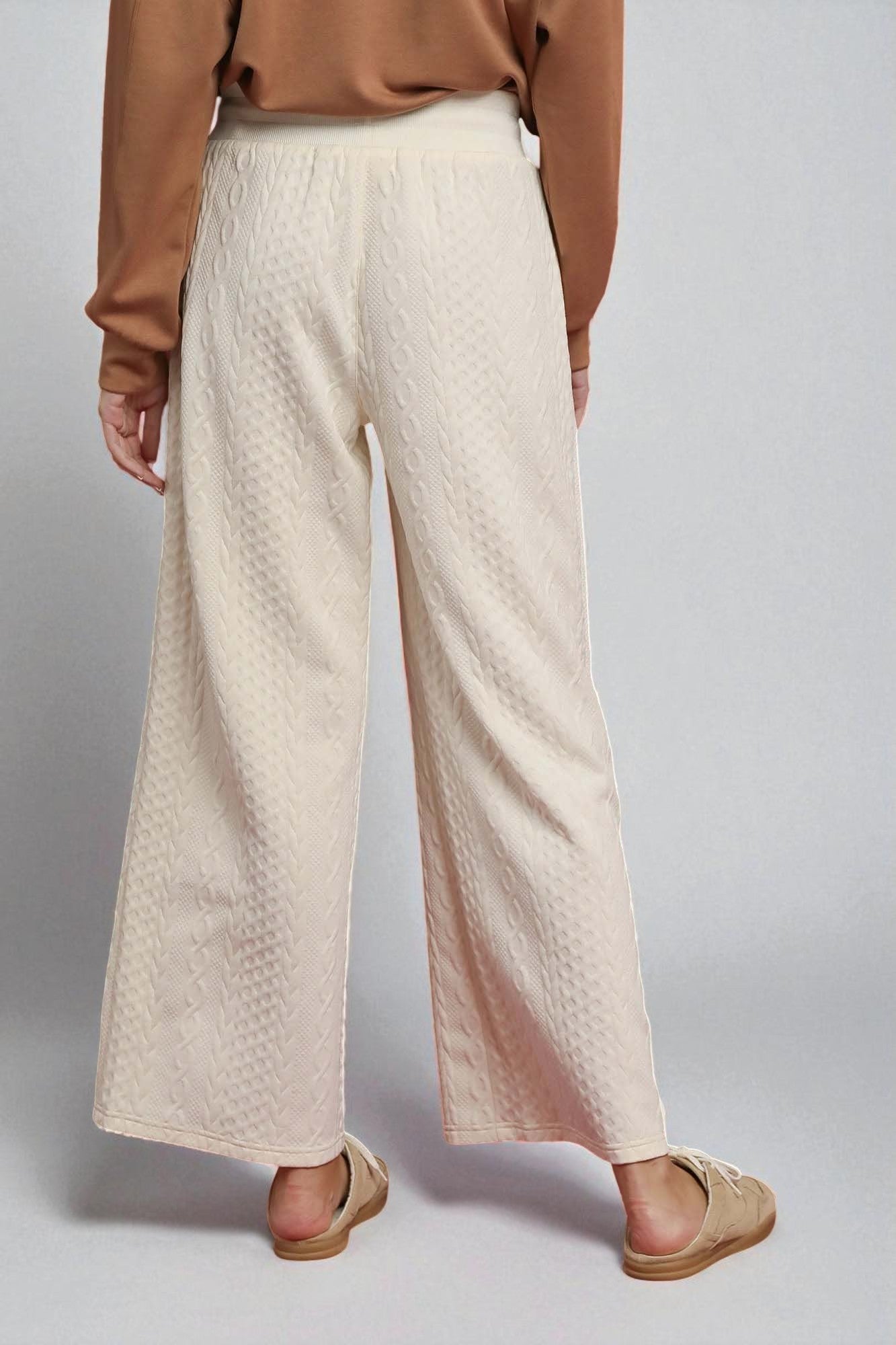 Person wearing beige textured pants and a brown top on a plain background