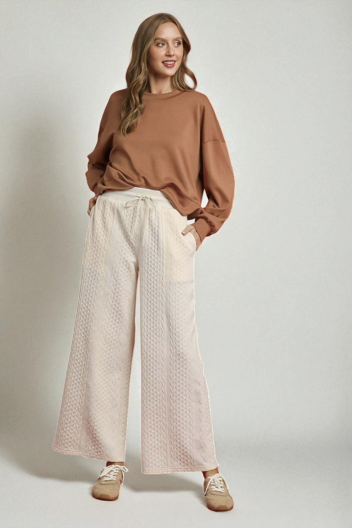 Woman wearing a brown top and beige patterned pants on a plain background