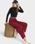 Person wearing a black top and red pants sitting on a wooden stool against a white background