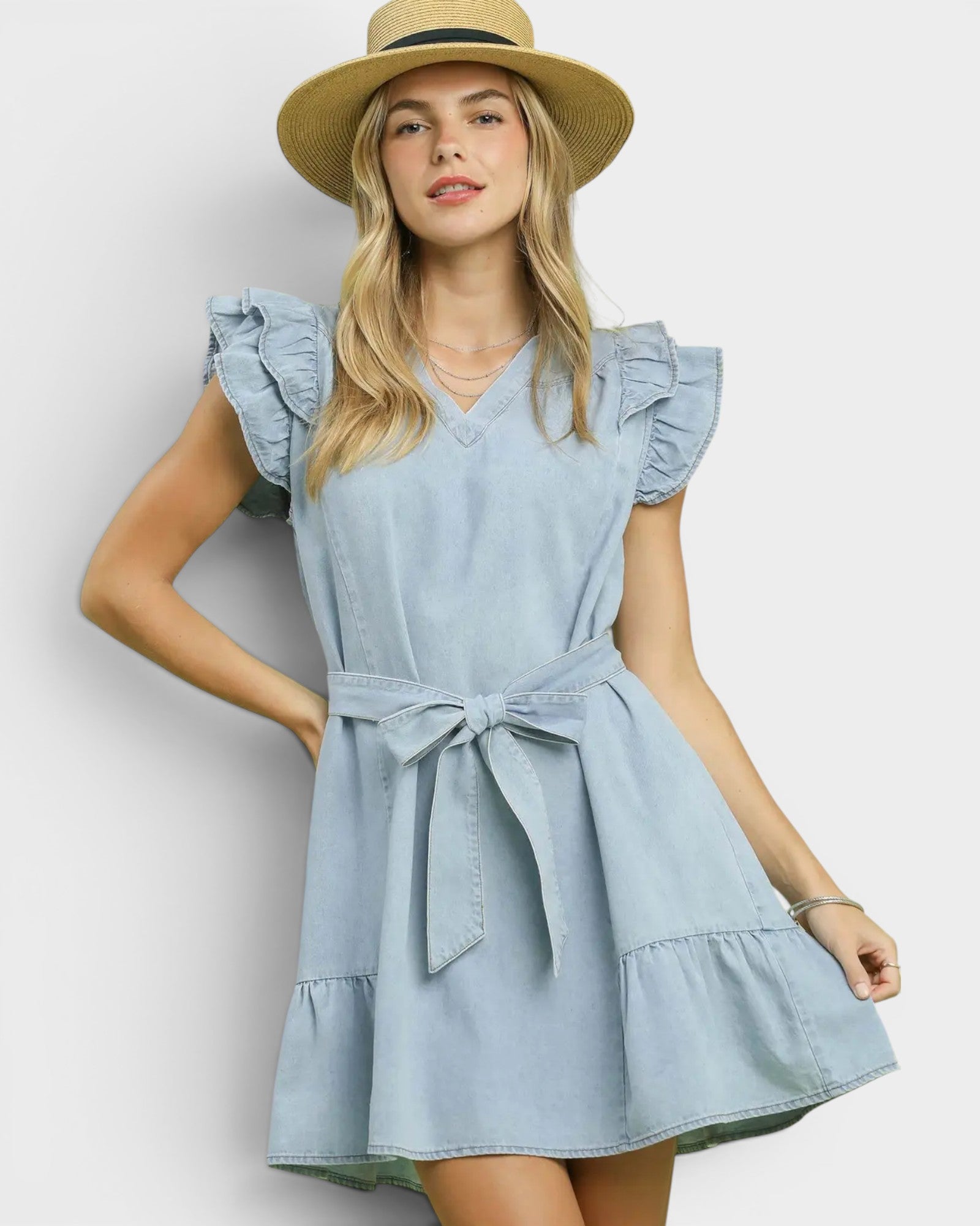 Woman wearing a light blue dress with ruffled sleeves and a belt, standing against a plain background.