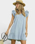 Woman wearing a light blue denim dress with ruffled sleeves and bottom hem, holding a straw bag against a white background.