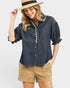 Woman wearing a denim shirt with ruffled sleeves and beige shorts on a white background