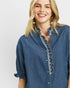 Woman wearing a blue denim shirt with lace details on a plain background