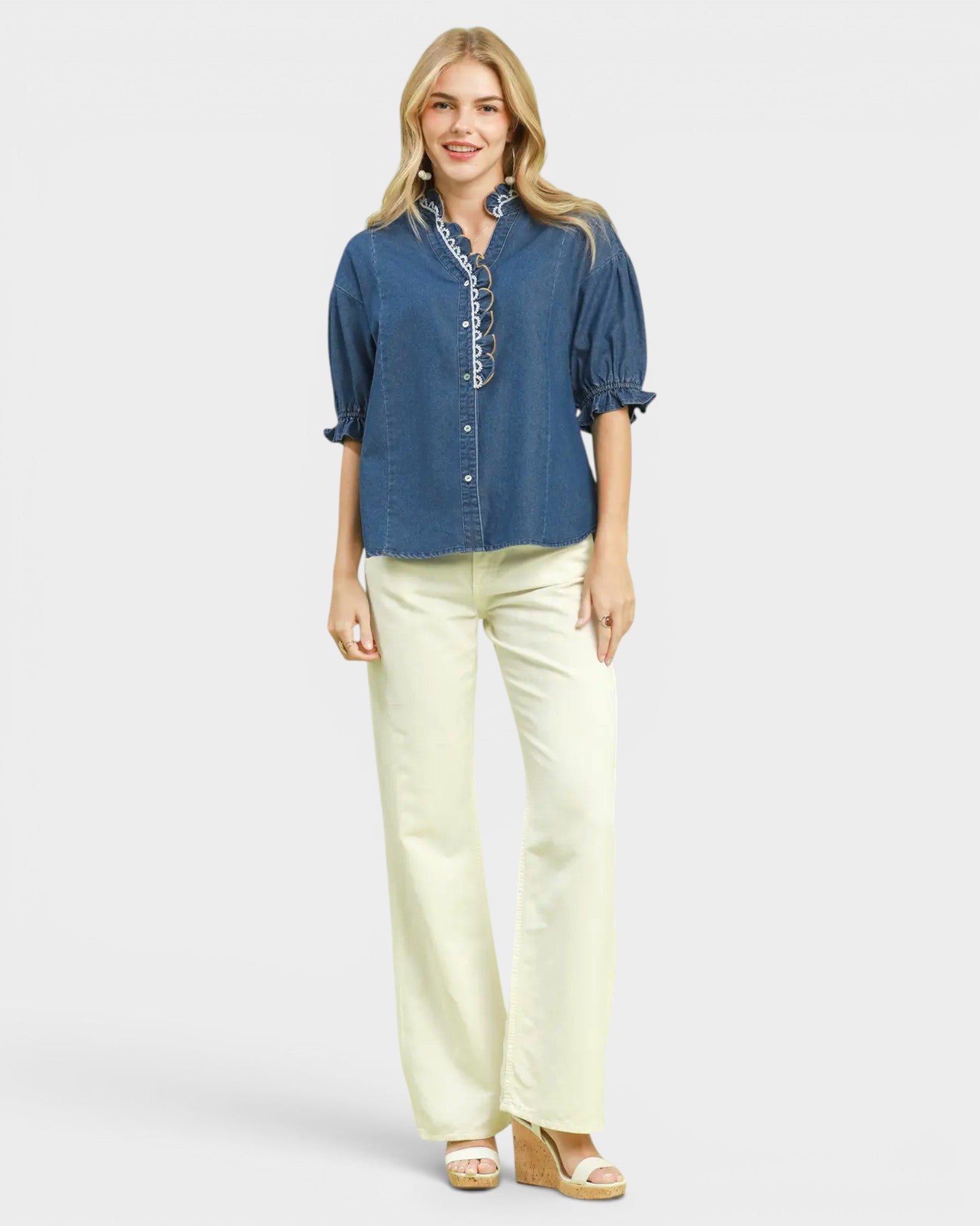 Woman wearing a blue denim shirt and light yellow pants on a white background